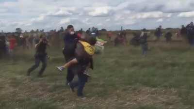 Hungarian journalist Petra Laszlo (blue shirt) trips a fleeing syrian refugee holding a child in an effort to get a good shot, causing him to be arrested by police. She was also taped kicking at other refugees