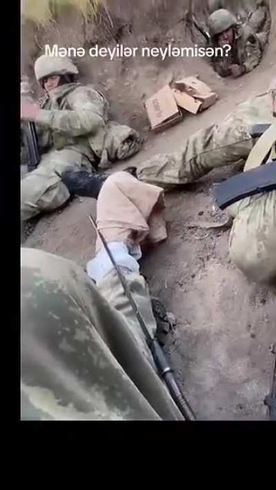 Soldiers lying in a trench as drones buzz overhead. One shaking from fear.