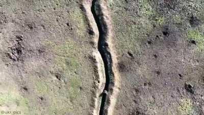 video showing a Ukrainian drone hitting a russian soldier moving along in the trench with a drone drop grenade. [music from source]