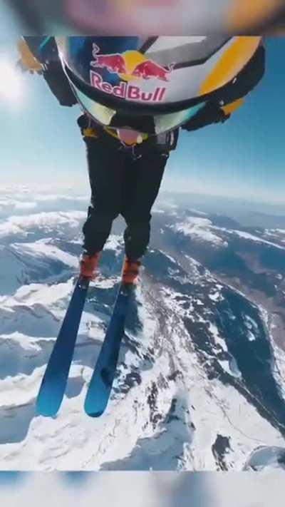 Cameraman (can see his shadow abut 24s in) keeping him in frame while managing his own parachute and skis while balancing himself