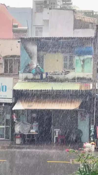 A Saigonese calmly covering her wears in response to a sudden downpour - during the rainy season downpours like this are common, so people have become very used to pausing and unpausing their operations at a moment’s notice