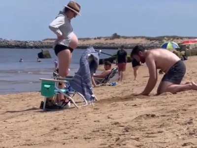 Husband digging a hole in sand for pregnant wife