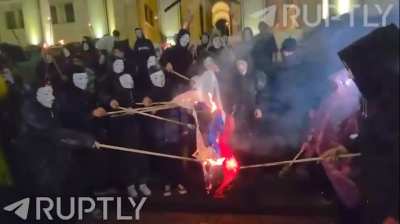 Act of protest in Georgia. People wearing Guy Fawkes masks burn the Russian flag in the street in protest against pro-russian candidates.
