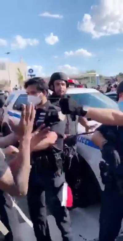 Black man with his hands in the air get his mask pulled down and pepper sprayed in the face