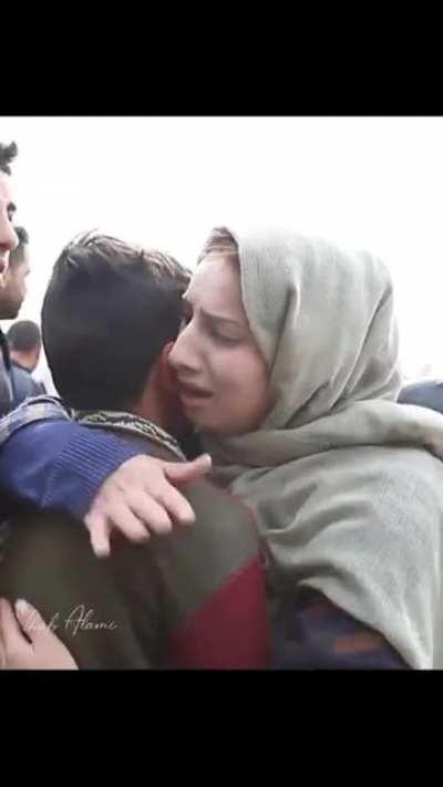 Mother cries while hugging her child as armed soldiers demolish their house in the background