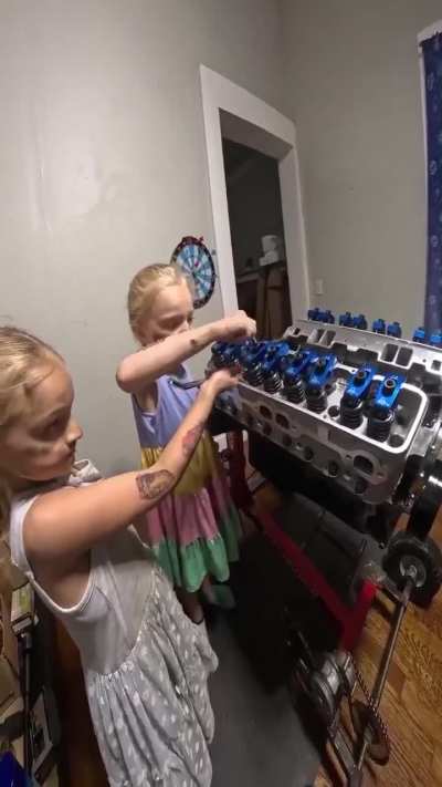 Two little girls helping their dad build an engine