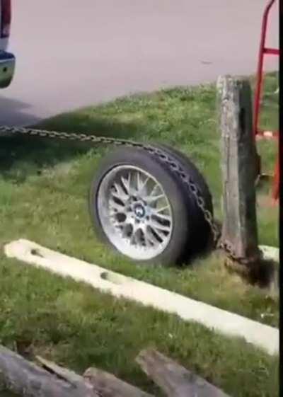 Pulling a post from the ground with a chain wrapped around a car wheel
