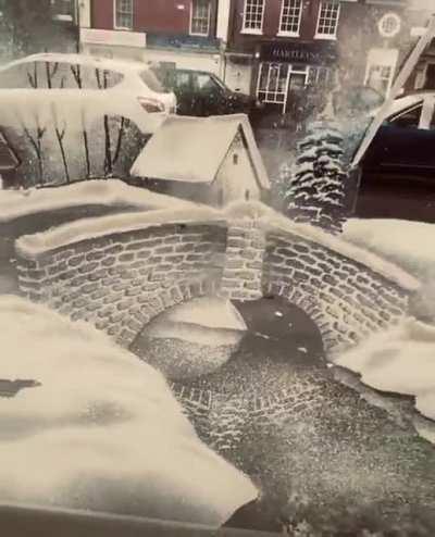 Artist uses snow spray on a window to create a snowy winter village