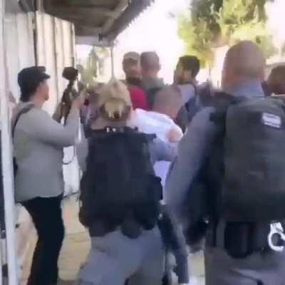 A man shields an elderly Palestinian woman from Israeli Occupation Forces who push them out to make way for Israelis participating in today's 