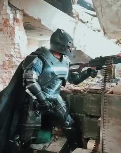 RU POV: A man in a Batman costume with the letter Z on his chest shoots from a PKM. Location unknown.