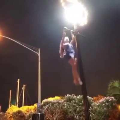 woman climbs up on the street light pole and does pull-ups.