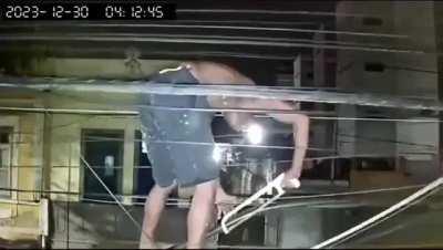 Man trying to steal cable from power line with a saw.