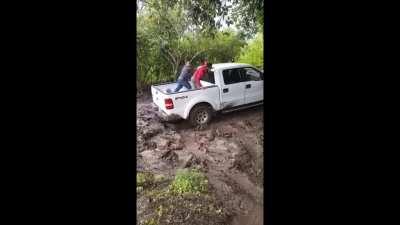 Workers attempting to push off a pickup truck that's stuck in mud