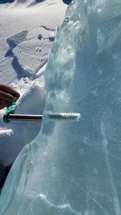 John Derting driving an ice screw into crystal-clear ice