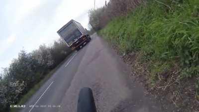 The oncoming truck overtakes tractor, almost hitting cyclist.