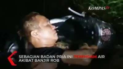 Seorang pria tertidur lelap dalam rendaman banjir rob