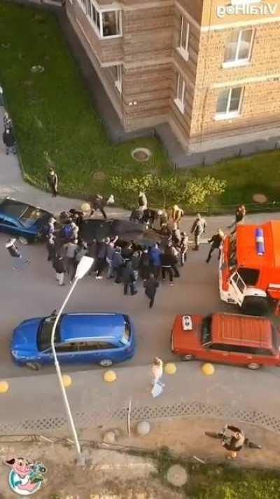 A group of guys use their man powers to ease a parked car out of the way of a fire truck on it's way to an emergency