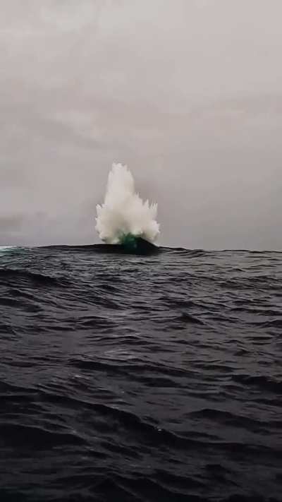 A powerful wave uprising due to small waves colliding to a big rock under water