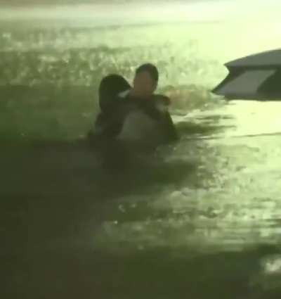 Weather reporter helps someone while reporting on flooding
