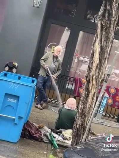 The owner of Foster Gwin Gallery sprays a homeless person with water in San Fransisco.
