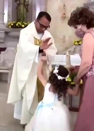 Kid gives high five to priest during blessing.