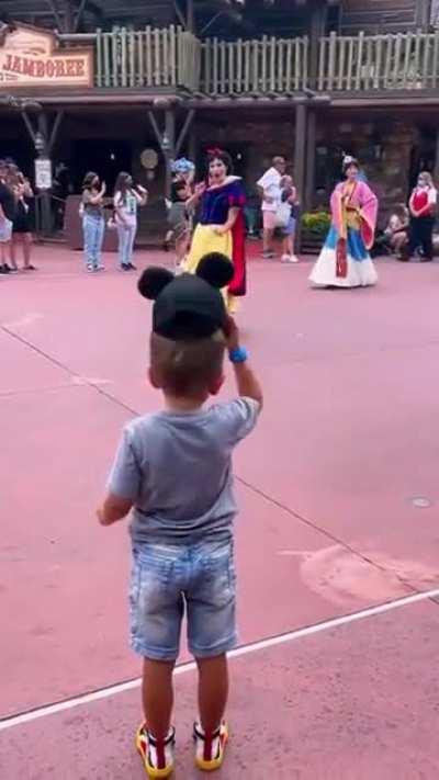 4-year-old boy tips his hat to Disney princesses during parade.