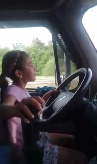 A 9 year old girl driving down a highway in a semi truck in Columbia.