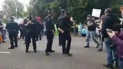 Policeman in Oregon flashing a white power sign at a Proud Boy