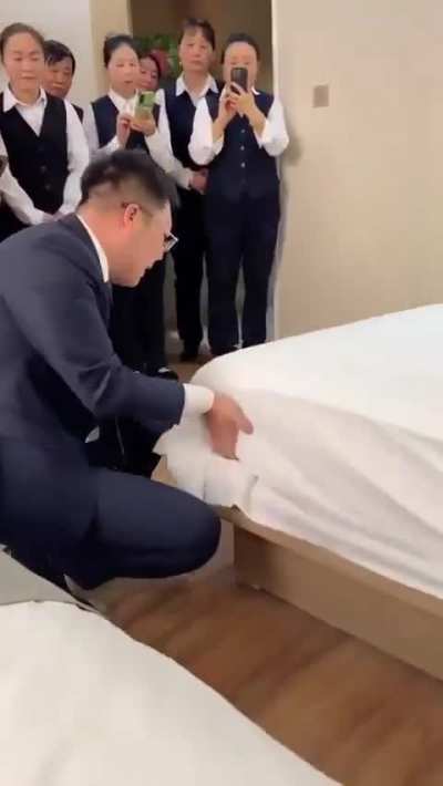 This man shows new hotel staff how to make a bed