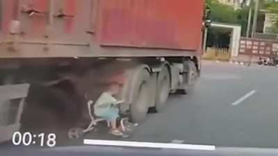 Crossing the road with his child by walking under a large truck