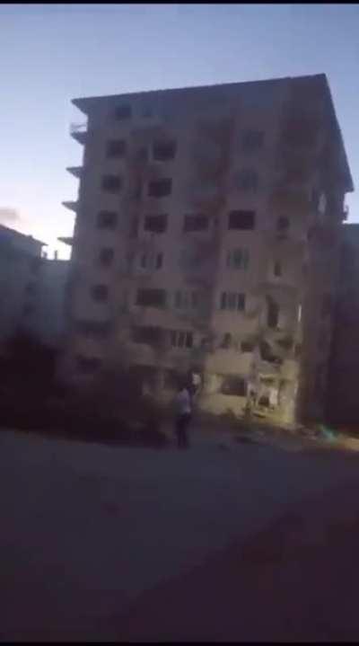 Man throws a rock to a damaged building.