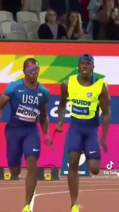 Blind sprinter in the Paralympics, David Brown, runs with his guide down the track as they cheer him on