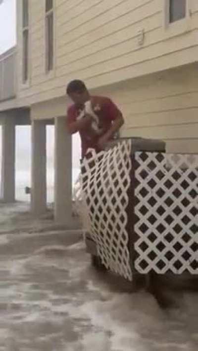A bro helps cat stuck on AC unit surrounded by flooding waters during Hurricane Ian.
