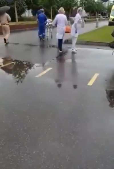 People stand in line waiting for the COVID vaccine as a man is transported by stretcher after an adverse reaction to the shot. Seemingly unaffected by the situation, they continue to wait in line, eager to gain access to special 