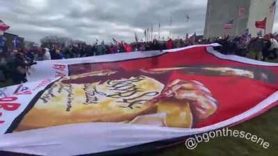 Trump supporters unfurl a giant flag depicting Nancy Pelosi shredding the Constitution outside the Washington Monument (Credit: Brendan Gutenschwager, Twitter)