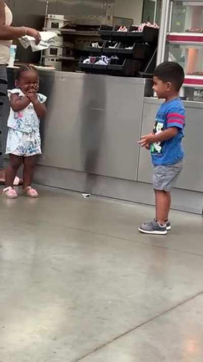 Little boy goofing around trying to get a smile from a little girl.