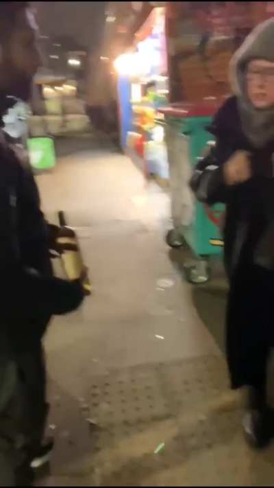 A woman shoplifts a bottle of wine in a store located in East London.