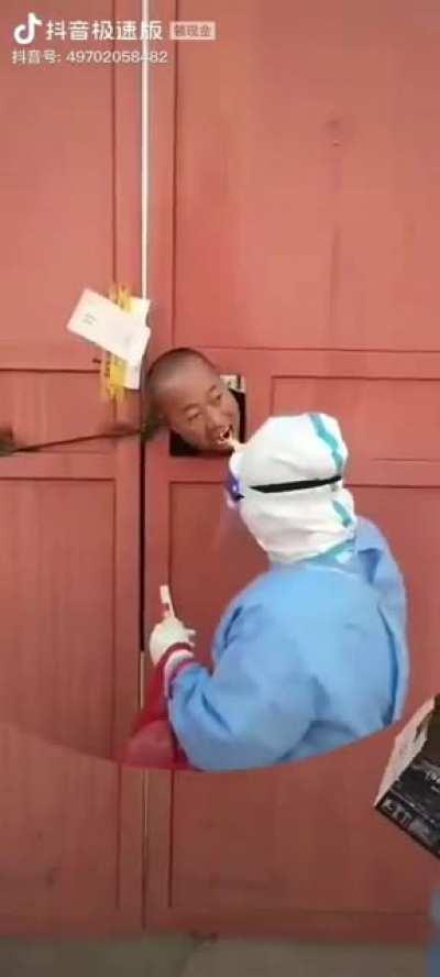 Authority going from door-to-door to test people in lockdown, through a hole in their doors , which were welded shut by authority. Hohhot, Inner Mongolia, China.
