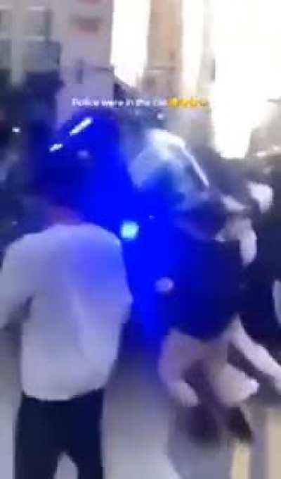 Rioters flipping over a police car with officers inside of it