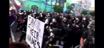 Police in Seattle snatch away a pink umbrella so they can pepper spray a peaceful protest crowd.