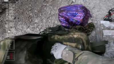 A Ukrainian soldier searches items from a KIA Russian soldier near his trench as artillery shells impact in background. 