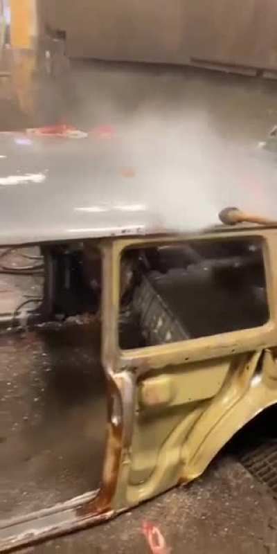 Powerwashing a cars body that's been dipped in paint stripper.