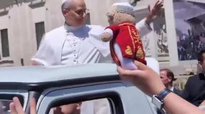 Pope Leo XIV in the Popemobile catching the mini Pope someone made him