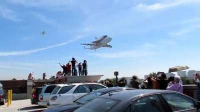 Shuttle Carrier Aircraft (SCA) N905NA, flanked by two F/A-18 Hornets on one side, makes a low pass while delivering the Shuttle Endeavor to LAX in 2012. This was N905NA's last shuttle delivery before being put on display at the Space Center in Houston.