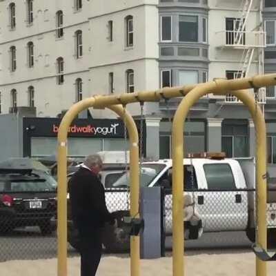 Just an old man pushing his dog on a swing