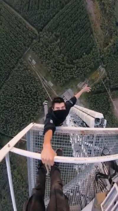 Guy hangs casually from high tower.