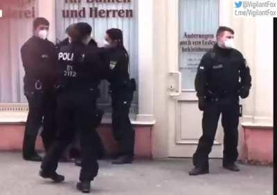 An elderly German woman walking her dog is stopped and questioned by police per COVID regulations. The woman challenges the ethics of these measures, calling them crazy, until officers gang up and arrest her. Is our 