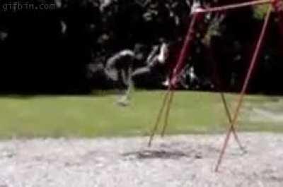 Standing directly in front of the kid on the swing