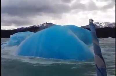 An aqua-blue iceberg emerging to the surface near a tourist boat off the coast of Argentina