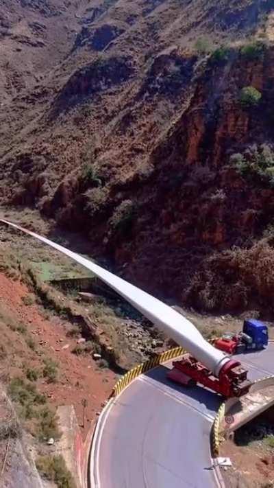 A giant wind turbine blade being transported through the mountains.